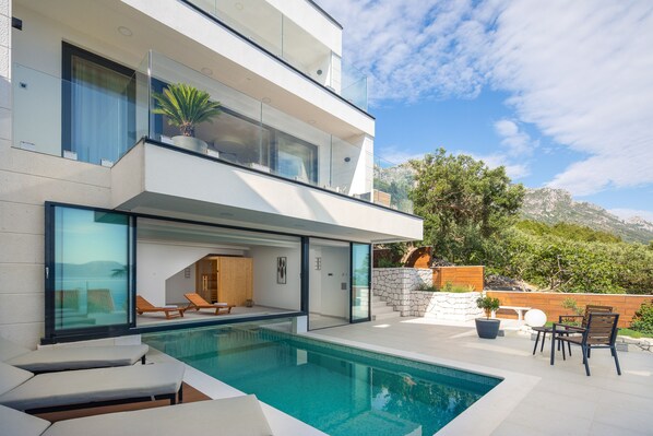 Une maison moderne à deux étages dotée d’une piscine, d’un espace salon extérieur et offrant une vue sur les montagnes.