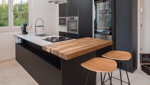 A modern kitchen with a central island, stainless steel appliances, and a large window. - LUXURY VILLA BLUE MOON (PODACA)
