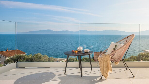 A balcony with a view of the sea, a table with a chair, and a small table with a teapot and fruit. - LUXURY VILLA BLUE MOON (PODACA)