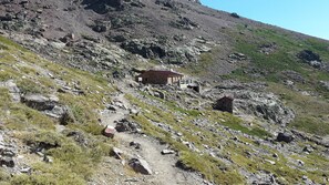A rugged mountain path with a small stone building, possibly a cabin, at the top.
