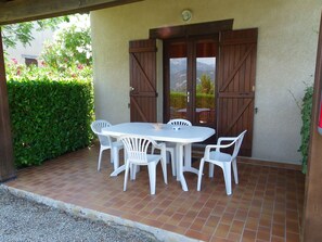 A patio with a white table and four chairs, a wooden door, and a view of mountains through the door.