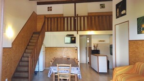 Un comedor con una escalera de madera, un televisor montado en la pared y una zona de cocina con refrigerador y microondas.