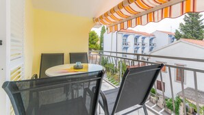 Un balcón con una mesa y sillas, un toldo a rayas y vistas a edificios con balcones.