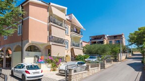 Un edificio residencial de varios pisos con balcones, un camino pavimentado y coches aparcados.