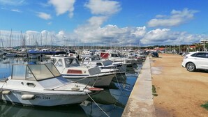 Un puerto deportivo con numerosas embarcaciones amarradas, un paseo marítimo de hormigón y cielo despejado.