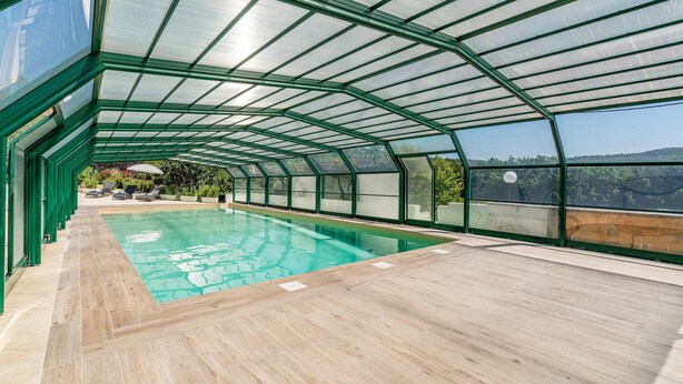 En overdækket swimmingpool med glasloft, træterrasse og udsigt over det omkringliggende landskab.