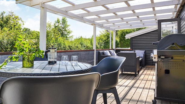 A covered outdoor patio with a table and chairs, a grill, and a view of a forested area. - 2 bedroom amazing home in Kirke Såby (Kirke Såby)
