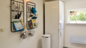 A kitchen with a white refrigerator, a window with a view of greenery, and wall-mounted storage racks with kitchen utensils and books. - 2 bedroom amazing home in Kirke Såby (Kirke Såby)