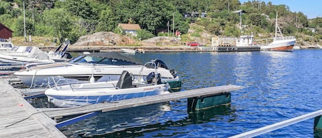 A marina with several boats docked, a wooden dock, and a backdrop of trees and hills.