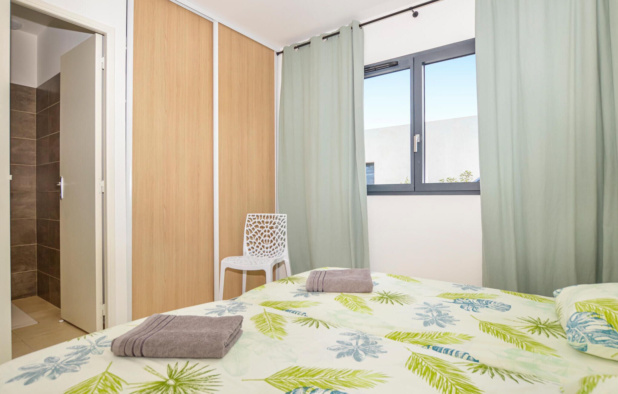 A bedroom with a bed, a chair, a window, and a door leading to a bathroom.