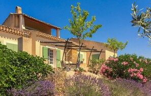 Ein traditionelles Haus im mediterranen Stil mit Ziegeldach, grünen Fensterläden und einer Pergola.