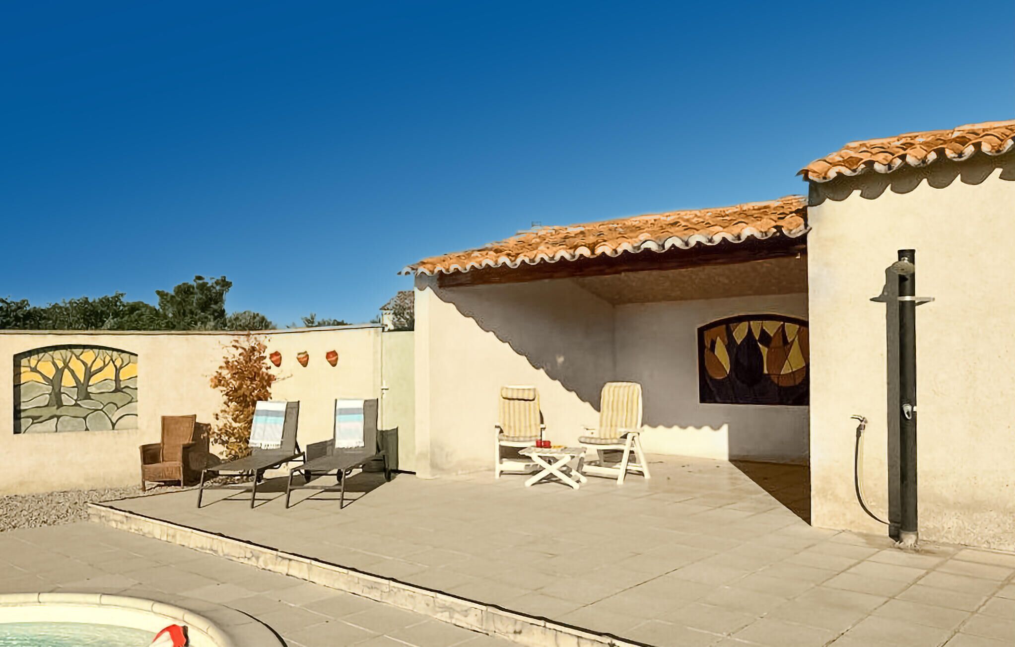 A poolside area with lounge chairs, a small table, and a decorative wall with a tree mural.