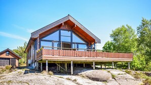 Ett modernt hus med ett stort glasfönster, en träveranda och en grund av sten.