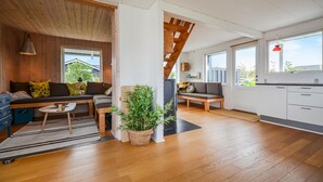 Un vaste espace de vie doté d’un plafond en bois, d’un canapé, d’une table à manger et d’un coin cuisine avec des placards et une fenêtre.