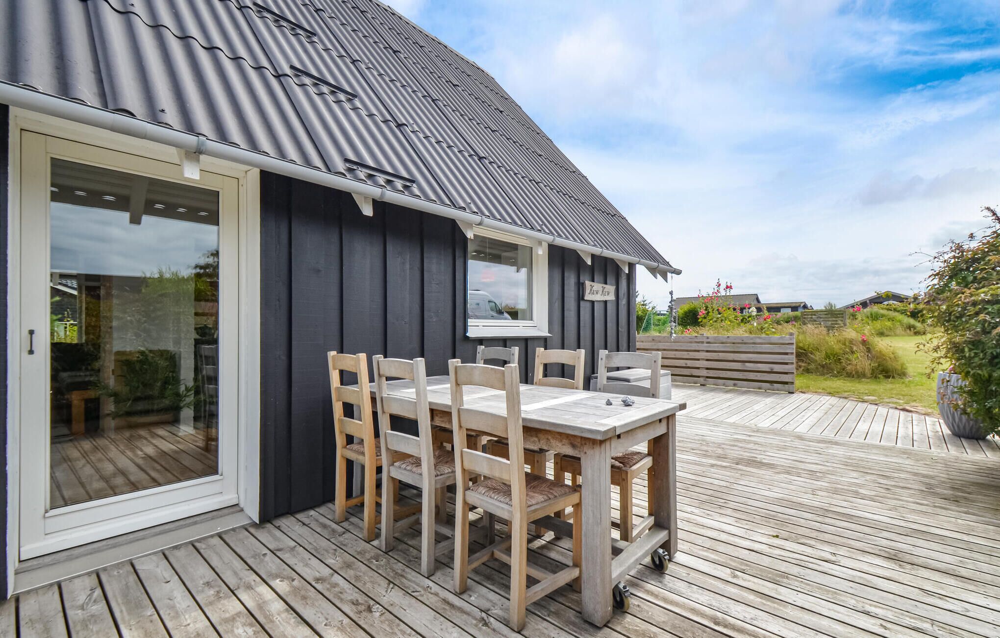 En træterrasse med et bord og stole, en skydedør og en bygning med mørke vægge og et metal tag.