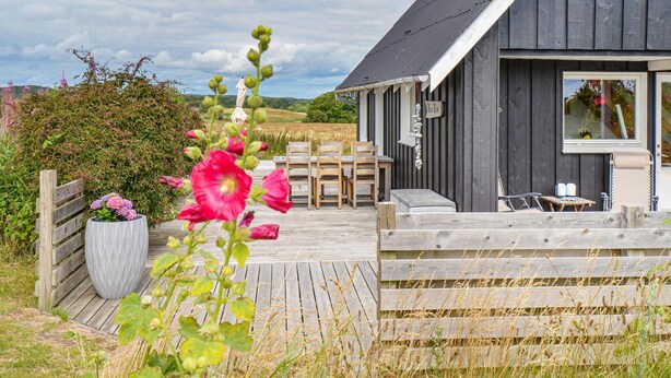 Une terrasse en bois avec des meubles d’extérieur, un grand bac à fleurs et un bâtiment à l’extérieur sombre, doté d’une fenêtre.