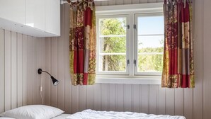 Un dormitorio con cama, ventana con cortinas, lámpara de pared y vistas a zonas verdes.