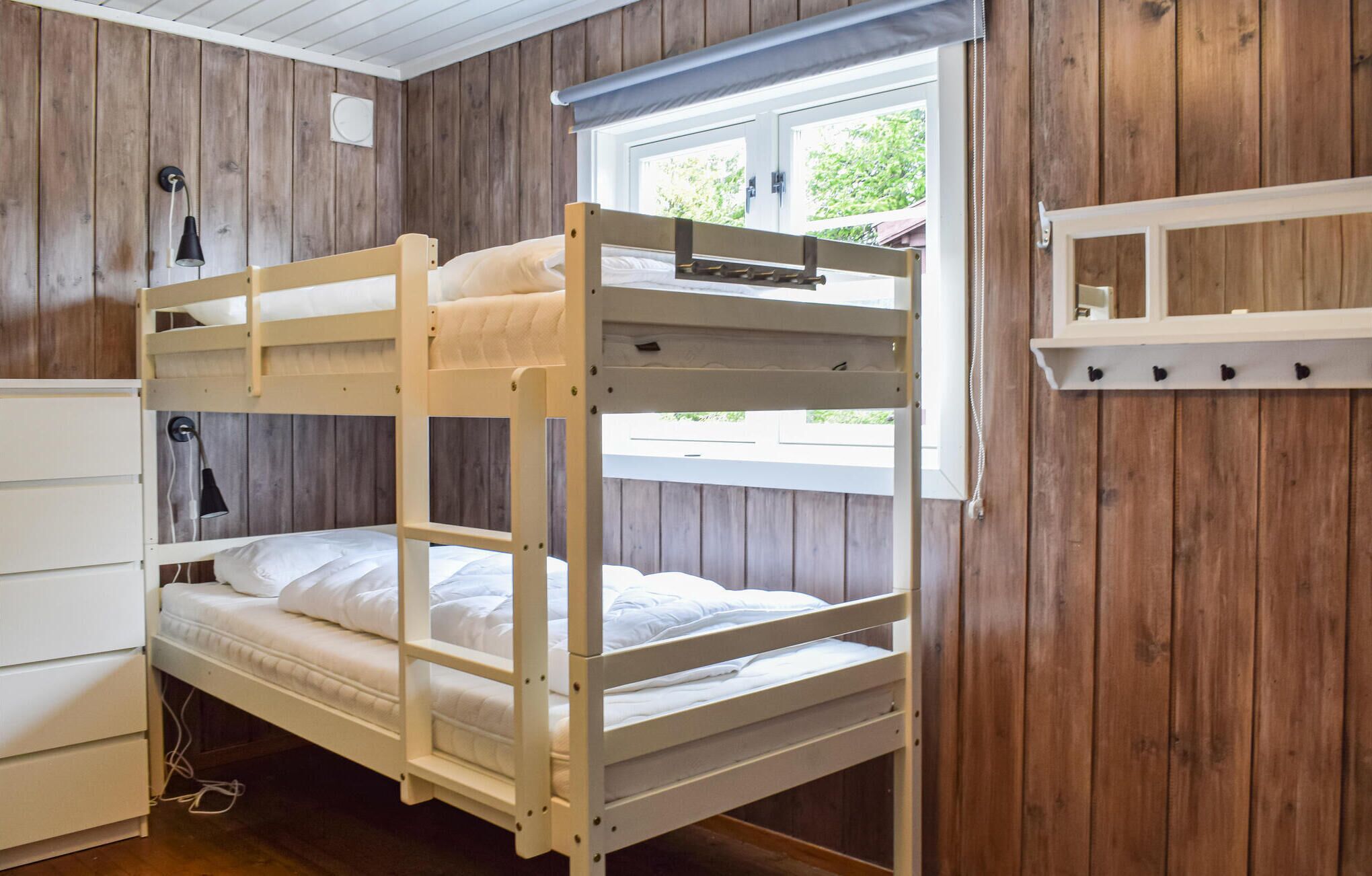 Dormitorio con literas, paredes de madera, una ventana y un aparador blanco.