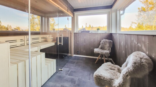 Un balcón moderno y bien iluminado, con puerta de vidrio, piso de madera y vista a árboles.