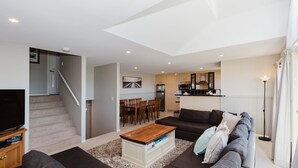 A modern living room with a flat-screen TV, a coffee table, and a sofa with cushions. A staircase leads to an upper floor. - Torino 7 - 7/14 Nettin Circuit (Jindabyne)