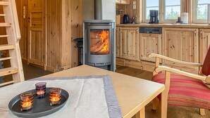 A cozy cabin interior with a wood stove, wooden cabinets, a dining table with candles, and a window with a view of trees. - Beautiful home in Sjusjoen (Sjusjøen)