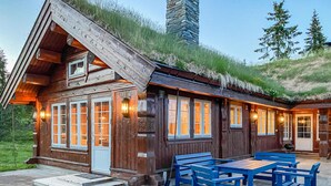 A wooden cabin with a thatched roof, large windows, and outdoor seating. - Beautiful home in Sjusjoen (Sjusjøen)