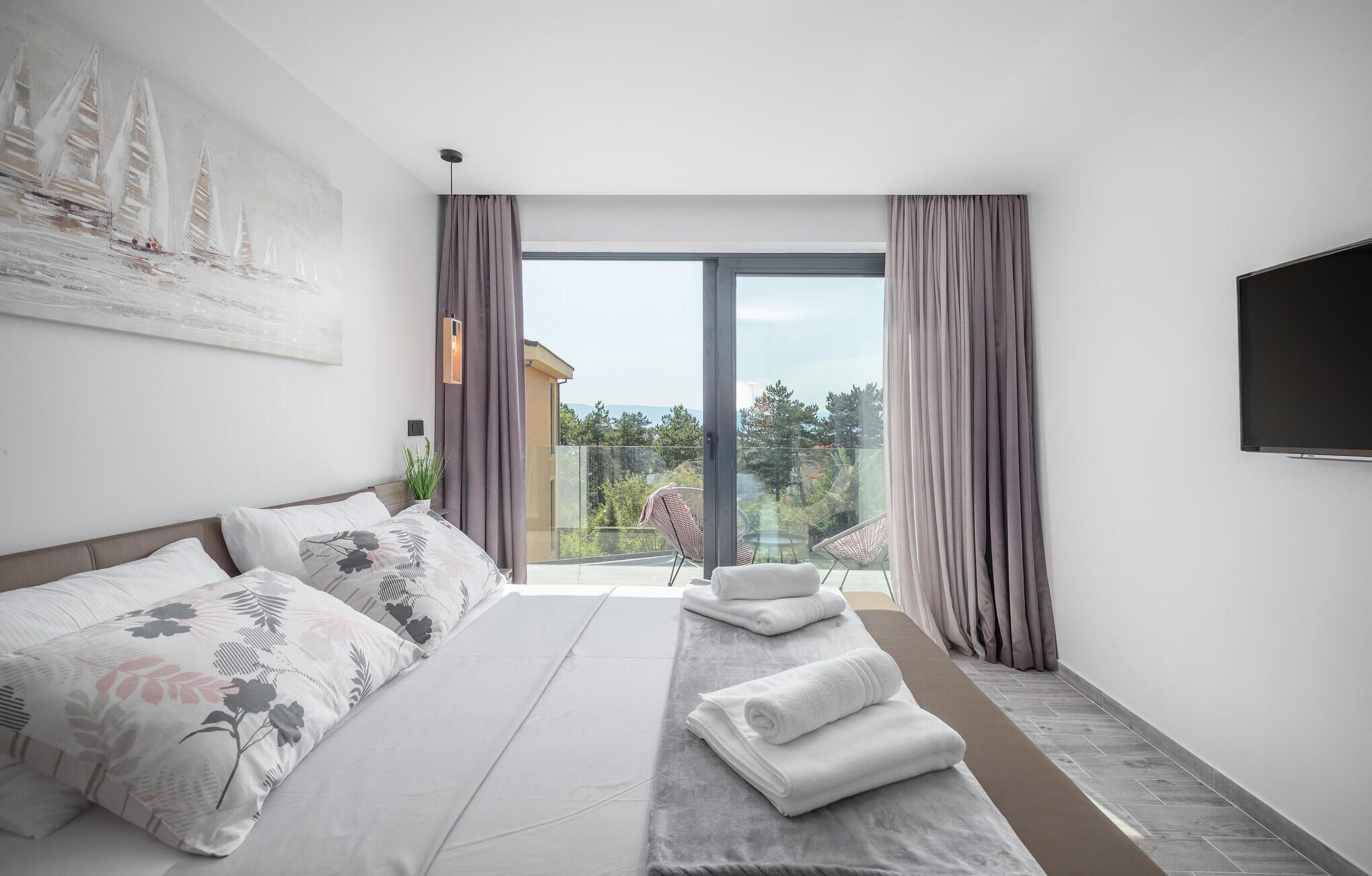 Une chambre d’hôtel moderne dotée d’un grand lit, d’une télévision à écran plat et d’un balcon offrant une vue sur le paysage.
