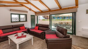 A living room with a brown sofa set, a white coffee table, and a glass door leading to an outdoor seating area. - Stunning home in Klek (Klek)