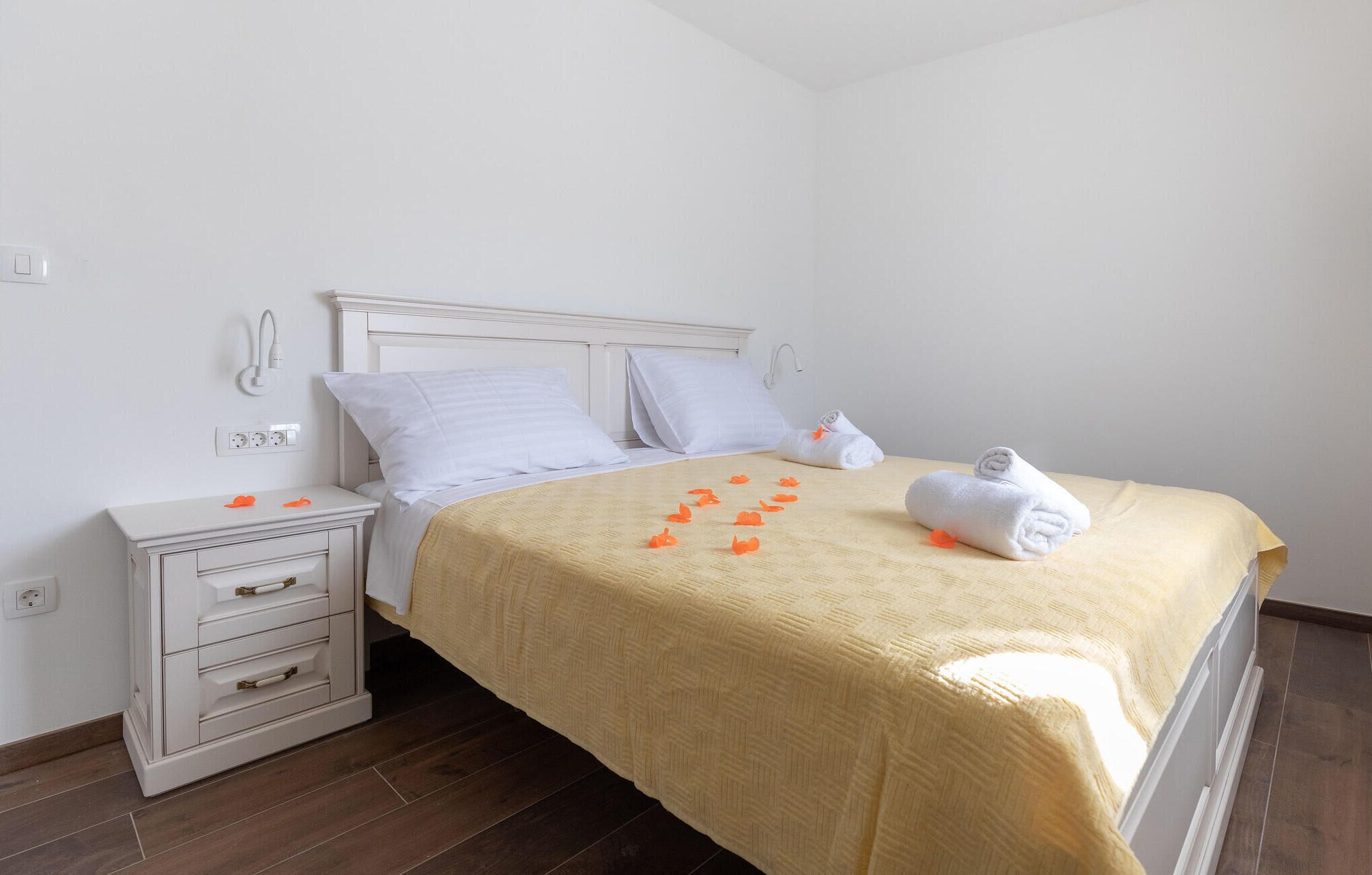 Una cama bien hecha con una colcha color crema, almohadas blancas y una toalla enrollada al lado.