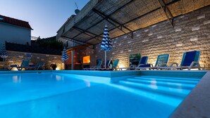 A swimming pool with lounge chairs and umbrellas, a stone wall, and a building with a tiled roof. - Stunning home in Klek (Klek)