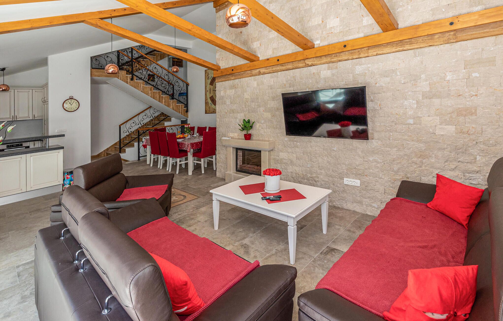 Un vaste espace de vie doté d’une cheminée, d’une table à manger avec des chaises rouges et d’un escalier menant à l’étage supérieur.
