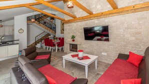 A spacious living area with a fireplace, a dining table with red chairs, and a staircase leading to an upper level. - Stunning home in Klek (Klek)