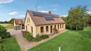 Ein gelbes Haus mit geneigtem Dach und Solaranlage, umgeben von einem gepflegten Rasen und Bäumen.