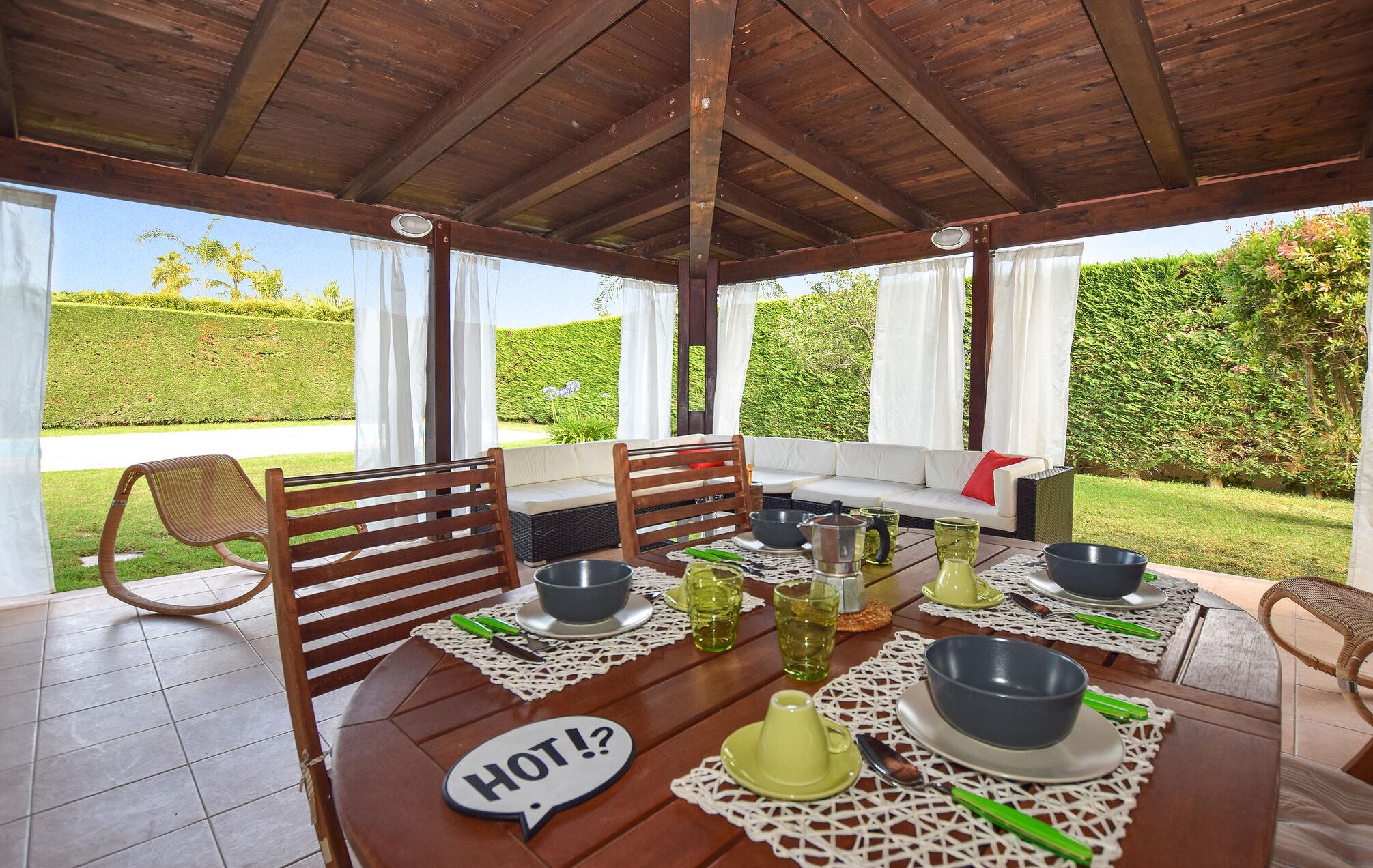 Un espace extérieur abrité, aménagé pour prendre les repas, avec une table pour deux personnes, un canapé et un fauteuil.