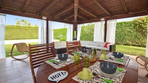 Zona pranzo all'aperto coperta, con tavolo apparecchiato per due, un divano e una sedia.