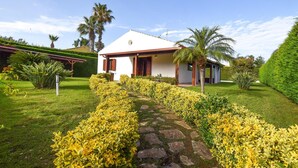 Una casa a un piano con facciata bianca e dettagli rossi, circondata da giardini curati e palme.