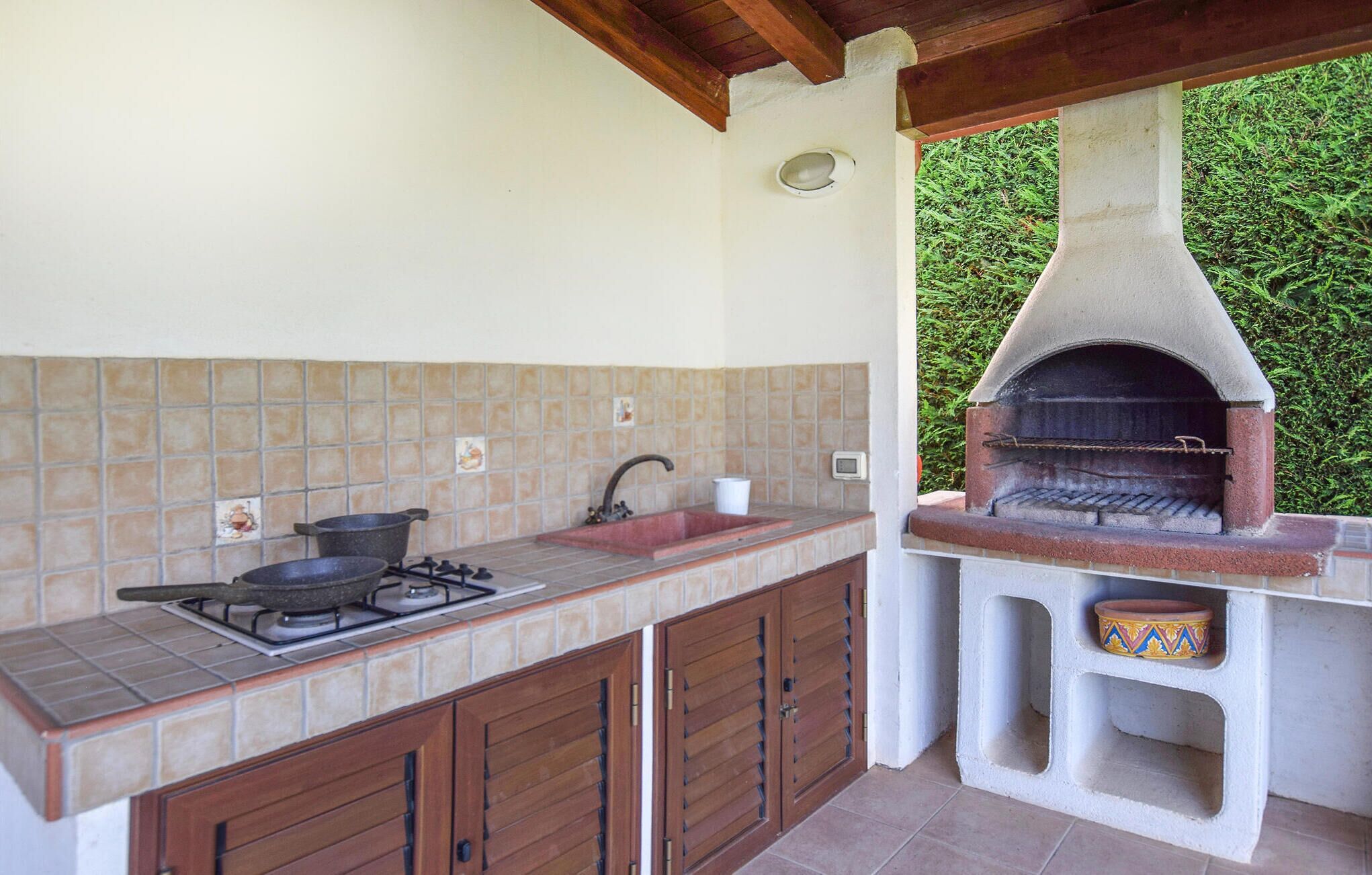 Een buitenkeuken met een gasfornuis, pannen, een spoelbak en een pizzaoven.