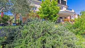 A Mediterranean-style villa with a garden, a large tree, and a clear blue sky.