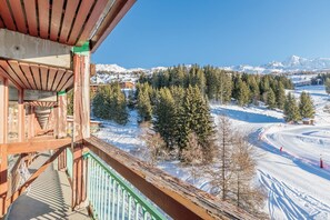 Un balcon en bois offrant une vue sur un paysage montagneux enneigé et une piste de ski.