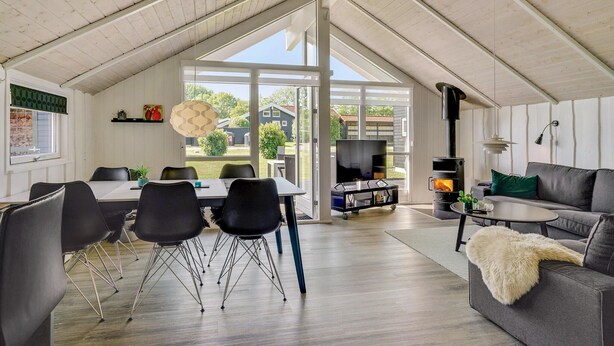 Uma sala de estar ampla com teto alto, uma mesa de jantar com cadeiras, um sofá e uma lareira.