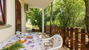 A covered outdoor patio with a table set for two, surrounded by a wooden fence and trees. - Awesome apartment in Valbandon with WiFi (Valbandon)