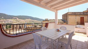 A balcony with a table and chairs, overlooking a mountainous landscape.