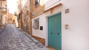 A narrow cobblestone street with a turquoise door and a metal gate on a white building.