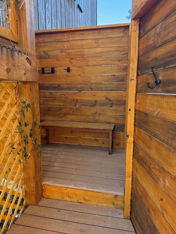 A wooden outdoor shower area with a bench, a wooden door, and a wooden fence.