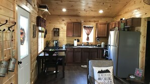Uma cozinha estilo cabana com paredes de madeira, uma geladeira, uma cafeteira e uma janela com cortinas.