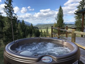 Een hottub op een houten terras met uitzicht op bergen en bomen.