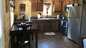 Cozinha no estilo cabana com paredes de madeira, geladeira de aço inoxidável, cafeteira e mesa de jantar com cadeiras.