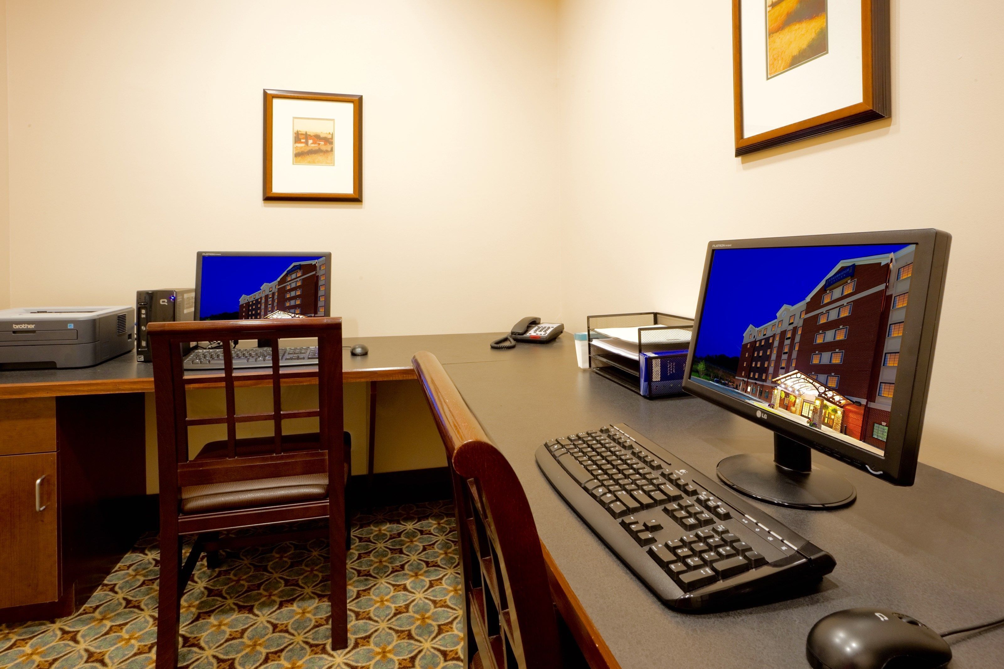 A hotel office with a desk, computer, keyboard, mouse, printer, and a chair.