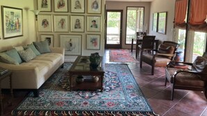 A spacious living room with a beige sofa, a coffee table, and a patterned rug. There are framed pictures on the wall and a dining area with chairs. - Beautiful Mountain Vacation Rental (Pipe Creek)