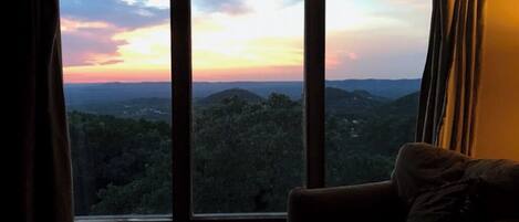 Une pièce dotée d’une grande fenêtre donnant sur un paysage montagneux au coucher du soleil.